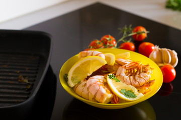 Food. Langoustines, induction stove, yellow plate, grill pan, tomatoes, lemon