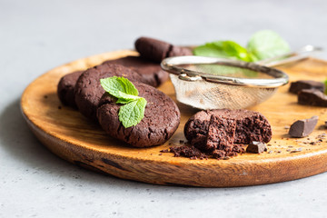 Chocolate cookies, pieces of chocolate, mint and cocoa powder on a wooden cutting board. 