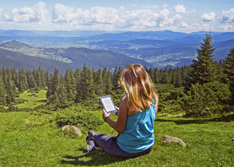Close-up of woman reading e-book in nature. Girl holding tablet computer screen which is editable isolated on forest background  in Dragobrat ,Carpathian mountains ,Ukraine