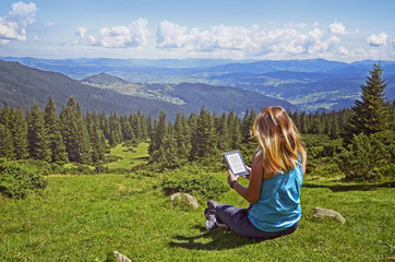 Close-up of woman reading e-book in nature. Girl holding tablet computer screen which is editable...