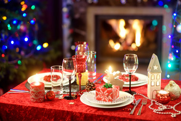 Beautiful table setting for Christmas party or New Year celebration at home. Cozy room with a fireplace and Christmas tree in a background.