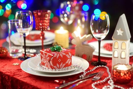 Beautiful table setting for Christmas party or New Year celebration at home. Cozy room with a fireplace and Christmas tree in a background.
