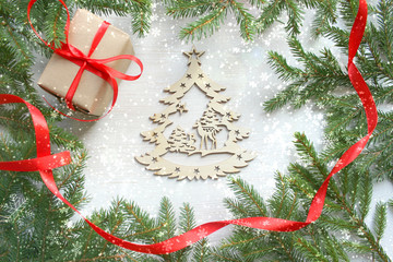 Christmas background. Green tree branches frame on white wooden background, gift box with red satin...