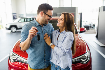 Beautiful young smiling couple holding a key of their new car.
