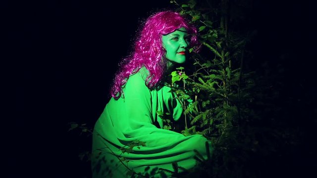 The green witch looks back in the bushes in the woods at night.