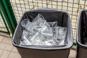 Big grey trach can full of used plastic transparent cups. Environment and world ocean pollution...