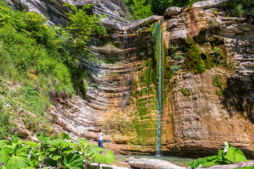 Woman near waterfall in mountain of Caucasus. Summer landscape with waterfall and woman in forest of Caucasus mountain. © Anton