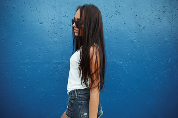 Girl on blue background.Sexy brunette in shorts and glasses