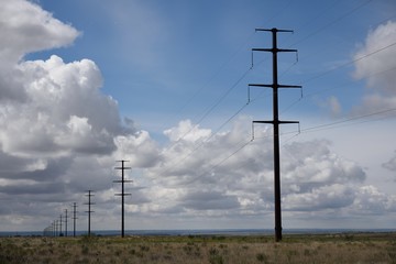 Long row of electricity transmission pylons against sky and clouds fading into empty rural landscape