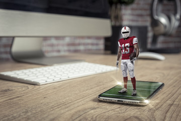 Football Player with a red uniform playing and coming out of a full screen phone on a wooden table.