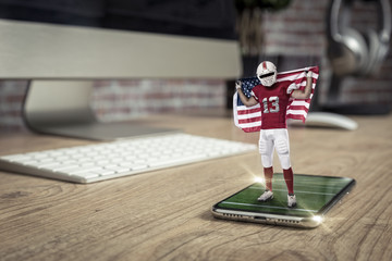 Football Player with a red uniform playing and coming out of a full screen phone on a wooden table.