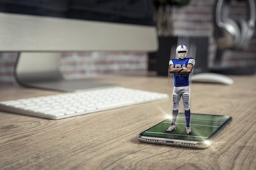 Football Player with a blue uniform playing and coming out of a full screen phone on a wooden table.