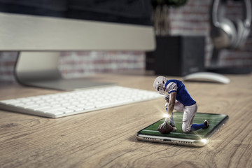 Football Player with a blue uniform playing and coming out of a full screen phone on a wooden table.