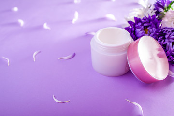 Jar with cream surrounded with flowers on purple background. Organic cosmetics. Bodycare