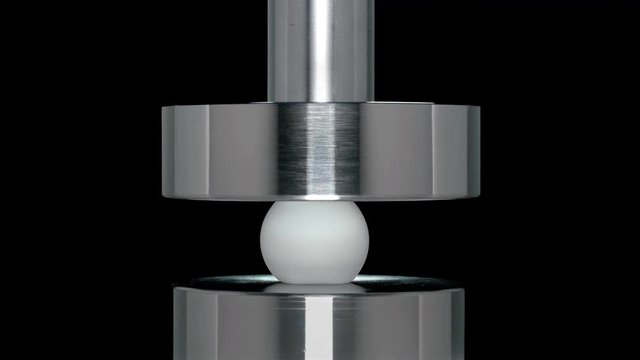 the ball from table tennis is crushed by hydraulic press, close-up