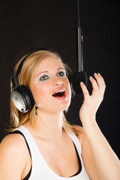 Woman singing to microphone wearing headphones in studio