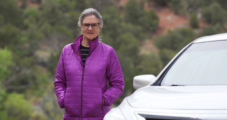 Somber elderly woman next to car looking at camera