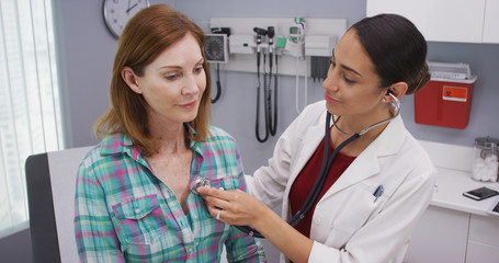Lovely young latina doctor using stethoscope to examine senior patients vitals. Charming hispanic...