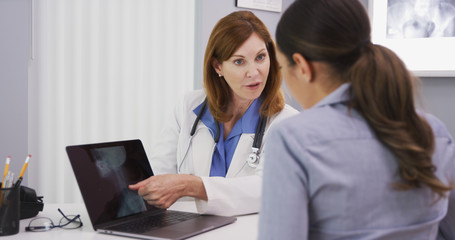 Obraz premium Portrait of senior medical doctor showing xray of spine neck and cranium to young female patient. Close up of young patient consulting with doctor over neck x ray