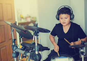 Asian boy put black tshirt and headphone learning and play electronic drum with wooden drumsticks