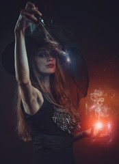 Young witch with a wand casting a spell in her ritual, halloween concept, makes a magical orb