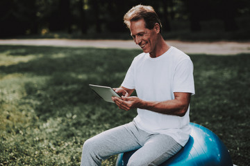 Obraz premium Man Sitting on Ball for Yoga and Using Tablet.