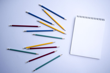 A white notebook with multicolored pencils is placed on a white background.