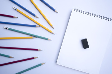 A white notebook with multicolored pencil and eraser is placed on a white background.