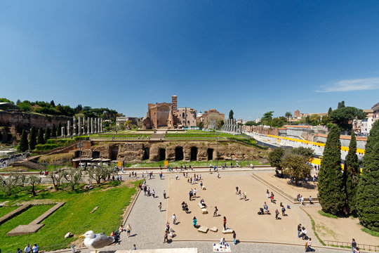 Roman Imperial Forum, in Rome, Italy, with Palatine Hill and unrecognizable tourists and a blue sky background