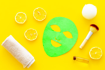Face spa products. Facial mask, cream, oil near lemon slices and towel on yellow background top view
