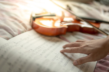 Musician hand on sheet of music note and vintage violin on flowery pink bed in the bedroom. Playing...