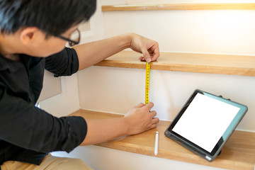 Young Asian worker using tape measure for measuring riser and thread on stair in the house. Writing...