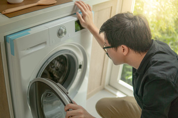 Obraz premium Asian technician looking into washing machine checking inside. Appliance maintenance in home laundry.