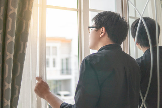 Asian man opening curtain looking out of the window. Home living lifestyle concept