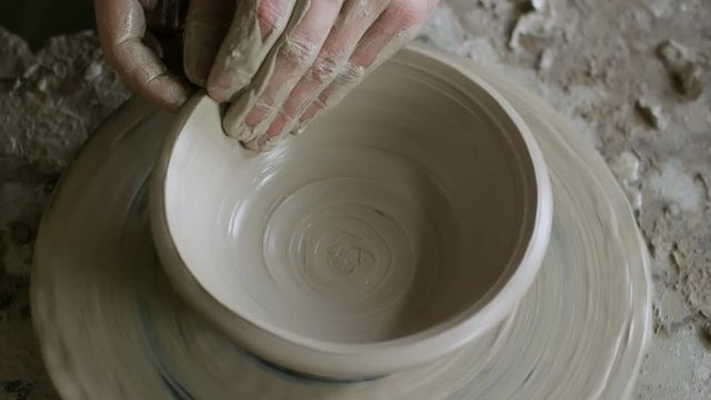 High angle shot with PAN of hands of unrecognizable pottery throwing bowl on spinning pottery wheel
