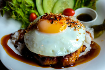 Zoom out of fried egg on hamburg with rice served in white plate on wooden table in cafe