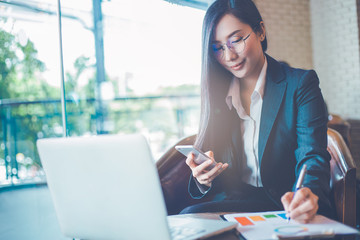 Business  woman asian uses a smartphone and writing on charts and graphs that show results.