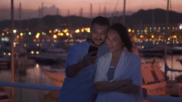Positive couple in love taking photos in the evening against harbour