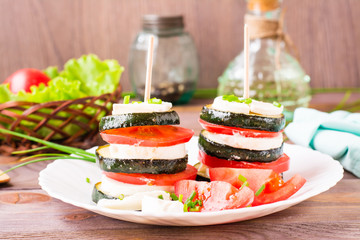 Original appetizer from fried zucchini, fresh tomatoes and feta cheese on a wooden skewer on a white plate