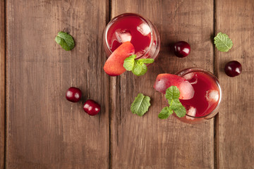 Overhead photo of vibrant red drinks with cherries on a rustic background