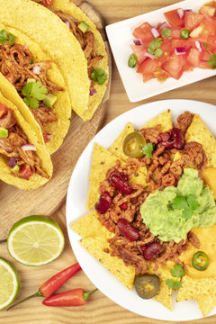 An overhead photo of Mexican tacos, pico de gallo, and nachos with chili con carne and guacamole