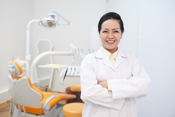 Portrait of female mature doctor in dental clinic folding arms and looking at camera