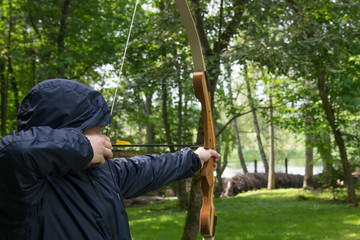 a man in a hood, pulls a bow string and takes aim at a shot at the target