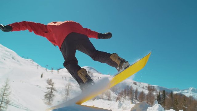 SLOW MOTION CLOSE UP: Extreme snowboarder jumping in big mountain ski resort. Detail of snowboard taking off the kicker in groomed snow park. Snowboarding jump on sunny winter day in snb park