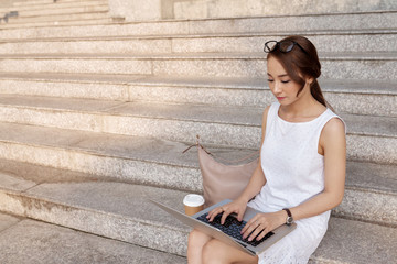 Fototapeta na wymiar Attractive charming Vietnamese woman sitting on steps and working on laptop