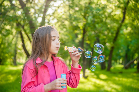 A little girl blowing soap bubbles in summer park