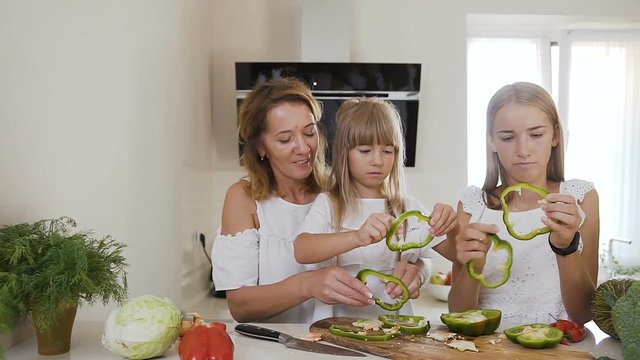 Mom teaches two kids daughters to cook at the kitchen table with raw green paprika at home in the kitchen. Mother teaching her daughters cutting vegetables in kitchen