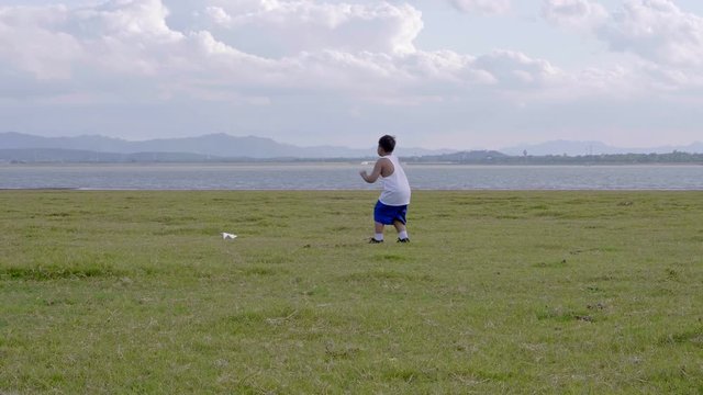 Little boy old 7 years Happy with a running and throwing paper airplane on meadow in summer in nature Sunset time. 4K Video Slow motion