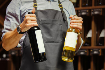 Young sommelier holding bottle of red wine in cellar
