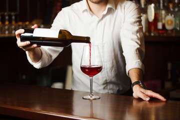 Male sommelier pouring red wine into long-stemmed wineglasses.